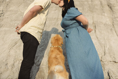 guy and girl kissing with shadows on the rocks and dog looking up at them