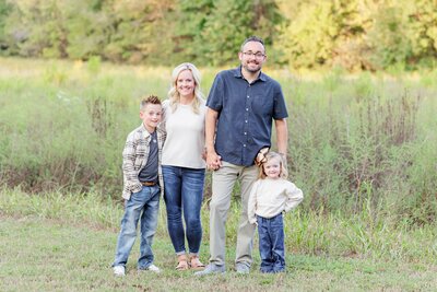 A family of four pose in a grass field for a family session.