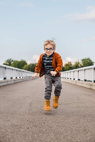 A young boy with glasses jumping mid-air on a bridge, captured by a Pittsburgh family photographer.
