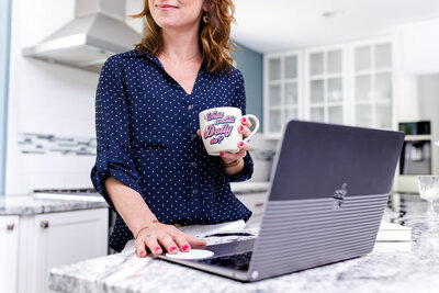 Girl standing behind an open laptop while holding a cup of coffee