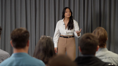 Trang Nova delivering a speech in front of a crowd wearing professional attire. 