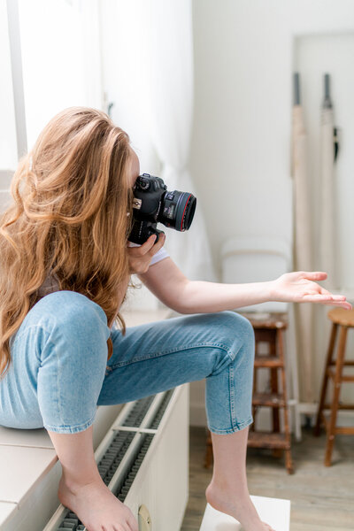 Behind the scenes fotograaf Isabeau Bosscher in actie. Vrouw met rood haar in spijkerbroek met camera.