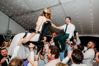 Flash photo of wedding guests holding bride and groom up on chairs at Dallas reception