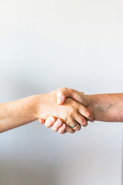 Close-up of two individuals shaking hands against a light background, representing trust, partnership, or business agreement