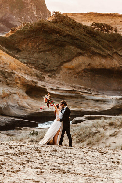 During their Oregon coast elopement, a couple shares their first kiss on top of a sandstone cliff looking out over the ocean