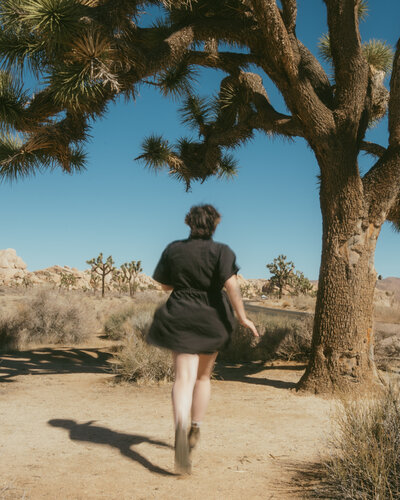 Running beneath a Joshua tree at sunset, hair flying and camera in hand, surrounded by desert glow