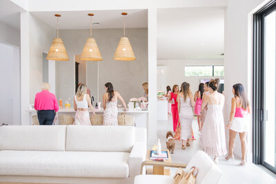 baby-63 Women gathered in a bright, modern kitchen wearing pink and white outfits during a celebration or event.