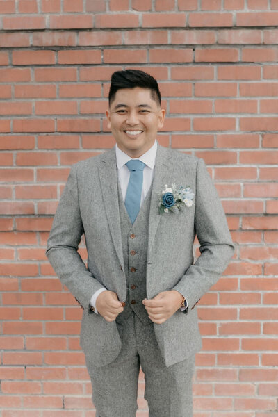 Millennial videographer smiling in a grey suit on his wedding day at The Junior League in Bakersfield, California.