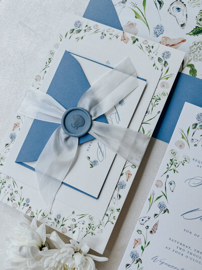 Orange, lemons, orange flowers, monarch butterflies in a woven basket with a Save the Date card and RSVP card present.
