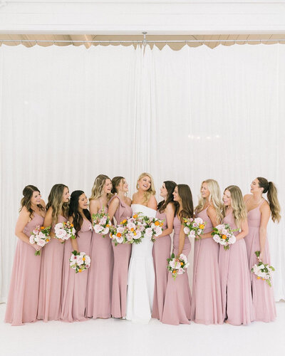 Bride and her bridesmaids posing for a photo looking at each other and smiling