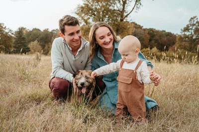 Toddler boy petting his dog while family explores a field during a Charlotte family photography session.