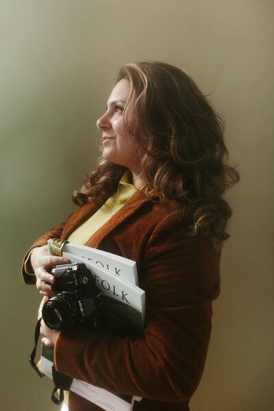 Sara Dobbins stands sideways holding her camera and Kinfolk magazines