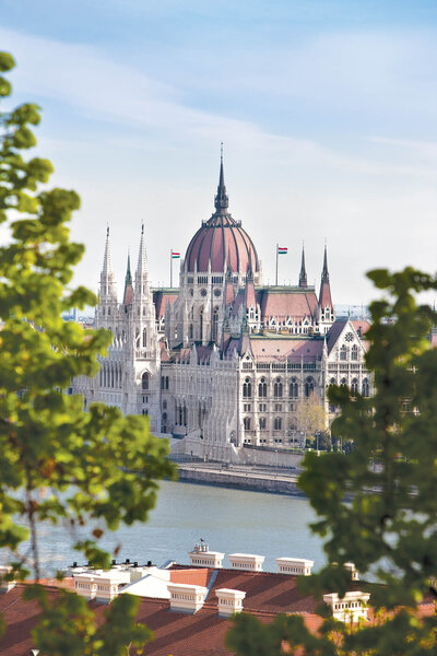 A grand riverside building with a large red-and-white dome and pointed spires, partially framed by green trees in the foreground.