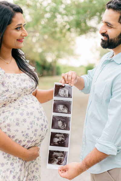 Couple smiles at each other while holding ultrasound photos during maternity photo session in Tampa, Florida