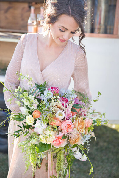 bride in a pink sparkly gown holding her bouquet looks down at her flowers