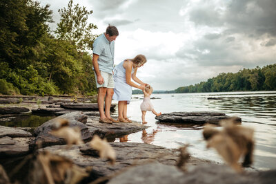 A mother and father explore a river with their baby. 