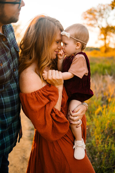 Captured by a family photographer in Albuquerque, this heartwarming image features a mom holding her beautiful baby dressed in a red outfit. The mom is stunning in a vintage orange dress, creating a timeless and vibrant family portrait.