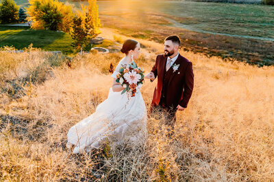 Bride and groom walking through a golden field at sunset Washington wedding photography by Aim True Photography