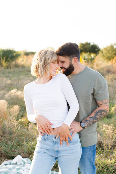 Couple holding each other at sunset in a tall grass field during their engagement session