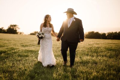 Bride and groom walk hand in hand during golden hour at their rustic barn wedding photographed by shelly voss photography.