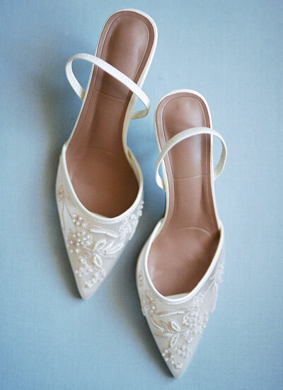 Detail shot of white wedding shoes on a baby blue background.