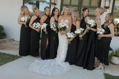 Bridesmaids in black looking at their bride and talking and laughing.