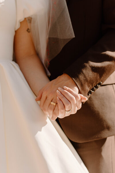 Up-close photo of the bride and groom holding hands and showing their rings