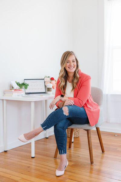 woman sitting and smiling in front of desk with computer, flowers and books