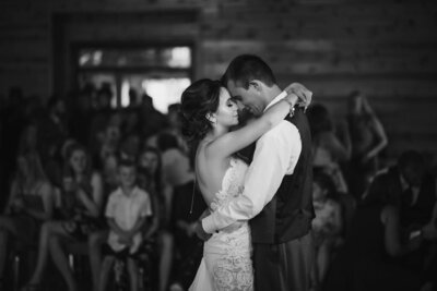 Young lovers enjoy the moment during their intimate first dance following their luxury wedding in front of friends and family. The photo is a moody and timeless black and white.