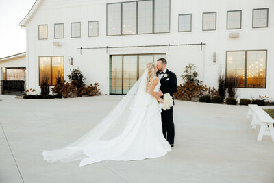 A bride and groom standing in front of their beautiful white barn wedding venue.
