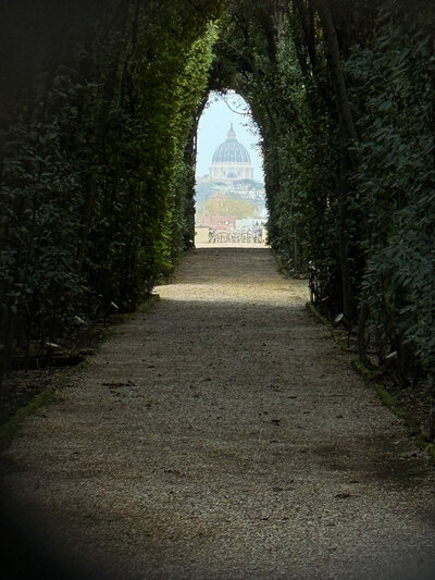 View of a hedge-lined pathway and St. Mark's Basilica through the Aventine Keyhole in Rome, Italy.