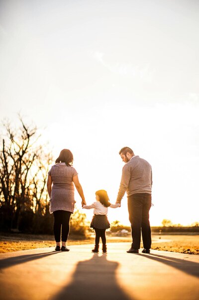 father and mother holding the hand of their daughter while walking in the sunset