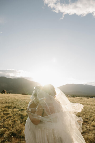 two brides standing in the colorado sunset with the veil over their heads
