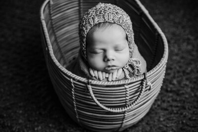 A serene image of a newborn boy sleeping soundly in a woven basket, surrounded by gentle fabrics.