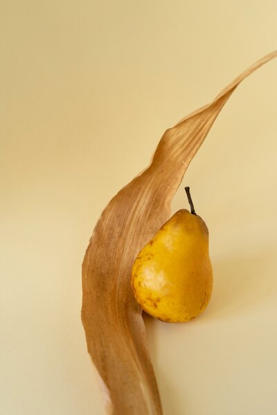 Pear and leaf sitting against a solid tan background