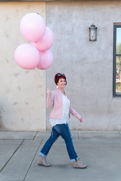 Woman walking with a bunch of large pink balloons as her Sacramento brand session prop.