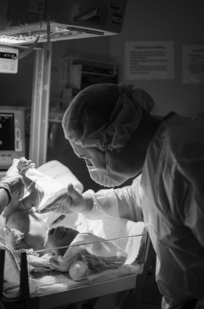 Dad in scrub meets infant daughter for the first time and shields her eyes from lights