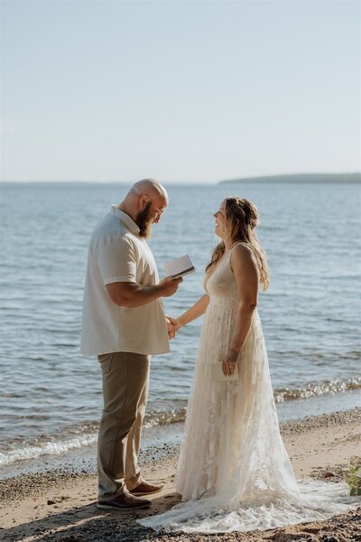 bride and groom saying their vows on a beach with a lake in the background