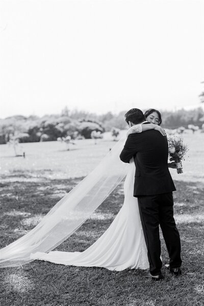 A newlywed couple hugging while one holds a bouquet of flowers 
