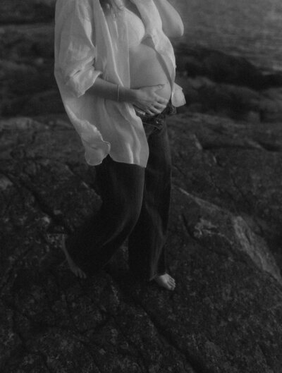 en gravid kvinna i jeans och skjorta går på klippor