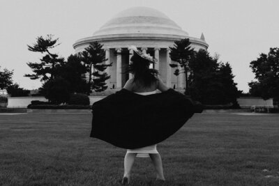 Black and white Graduation photo of a girl in her cap and gown in front of a college building spinning around