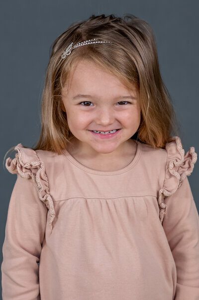 Preschool girl in a pink ruffle dress smiles for her fall school photos