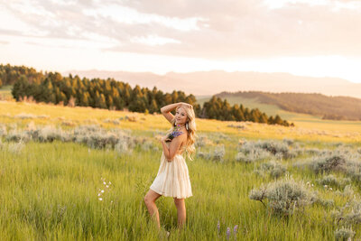 Young woman runs her fingers though her hair as she holds a wildflower bouquet in the tree-linedmoutains.