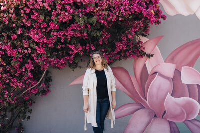Owner of Woodall Creative Co stands in front of mural of pink flowers with a tree of pink flowers framing her.