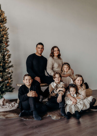 A young family with five children pose near her a Christmas tree while dressed in their Sunday best.