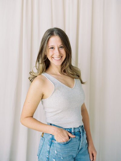 Studio portrait of a woman in a tank top and jeans on a cream background