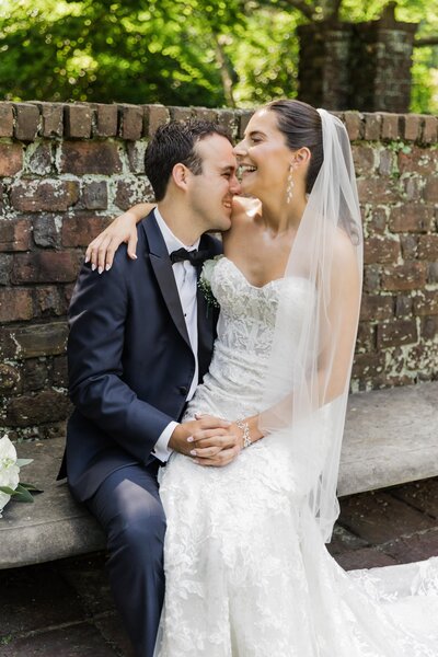 Bride sitting on Groom's Lap in front of a stone wall