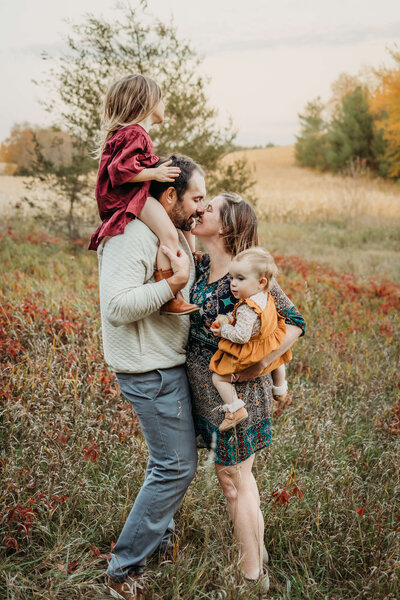 family fall portraits in field while mom and dad kiss near eau claire wi