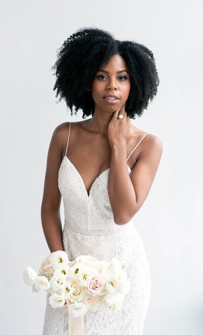 Editorial bridal portrait of a black bride with natural curly hair showing off her wedding ring and bridal bouquet.