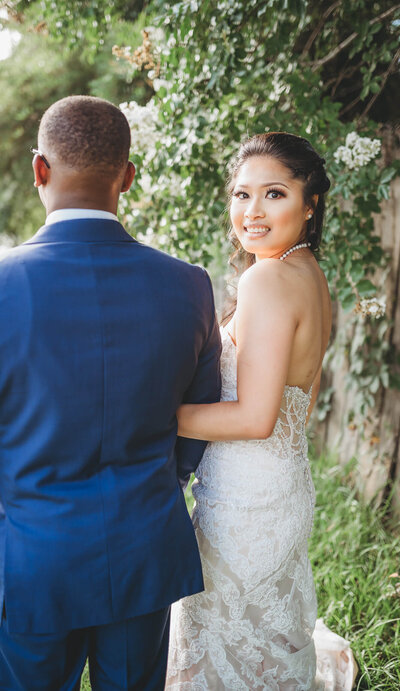 Bride smiles while holding groom’s arm in a lush outdoor setting. Captured by Jackson Ms Wedding Photographer.